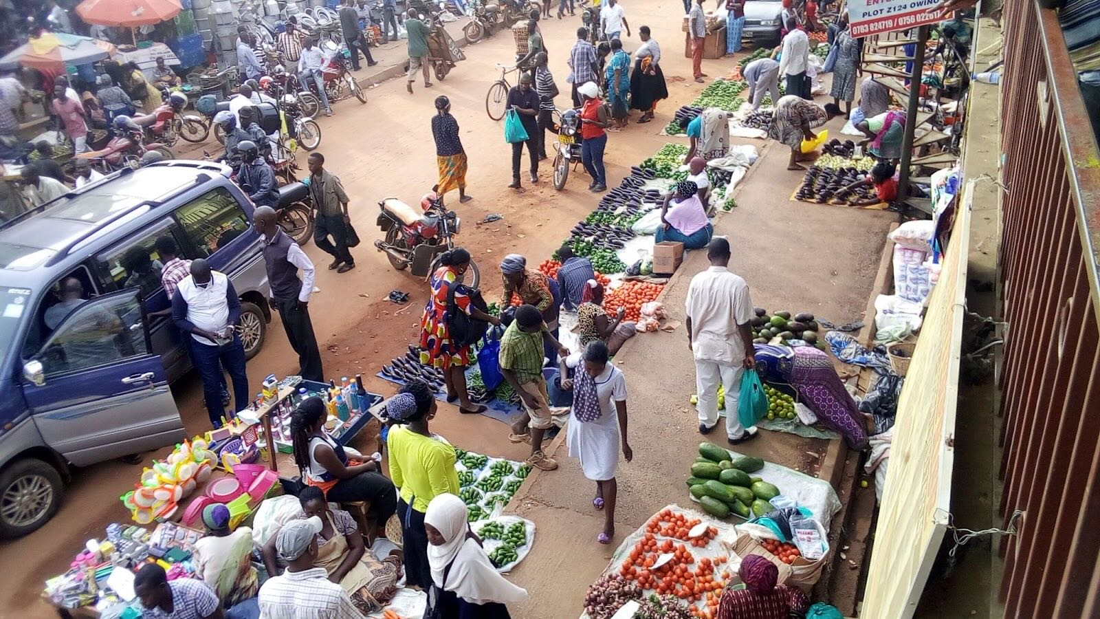 Street vendors are set up outdoors in markets in Kampala, Uganda, many displaying their colorful produce on covered ground. 