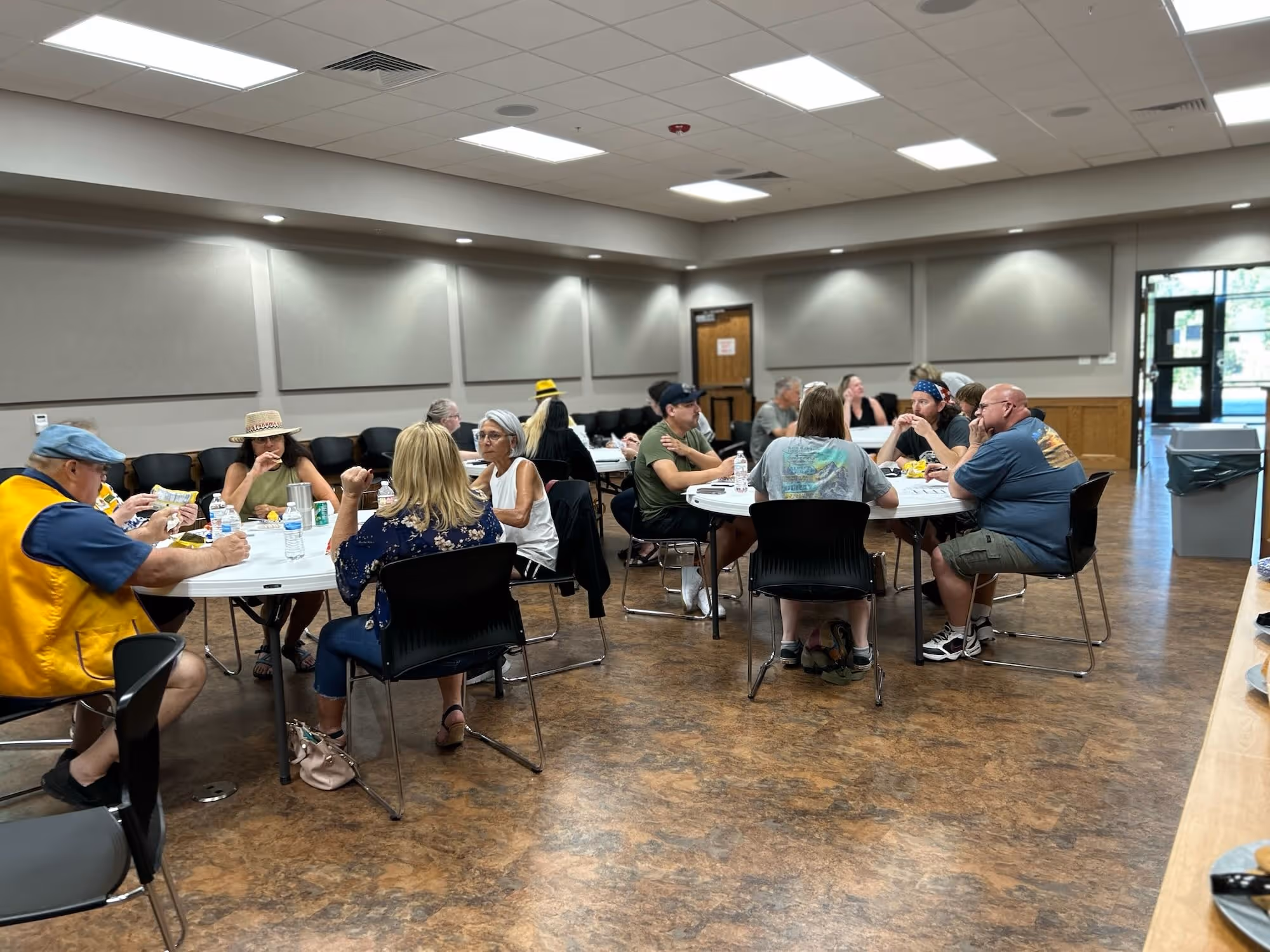 Individuals sit at round tables in an indoor setting, eating and talking.