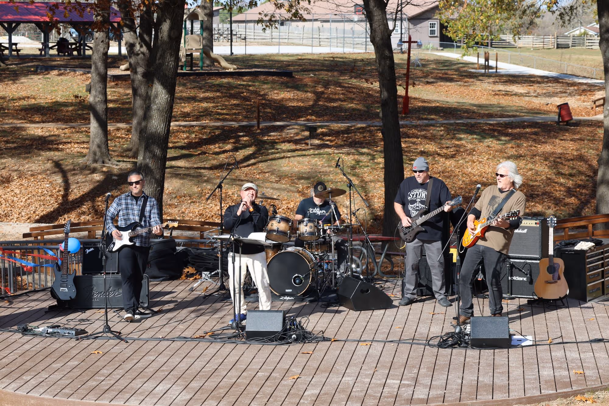 Five musicians perform on an outdoor stage in a park