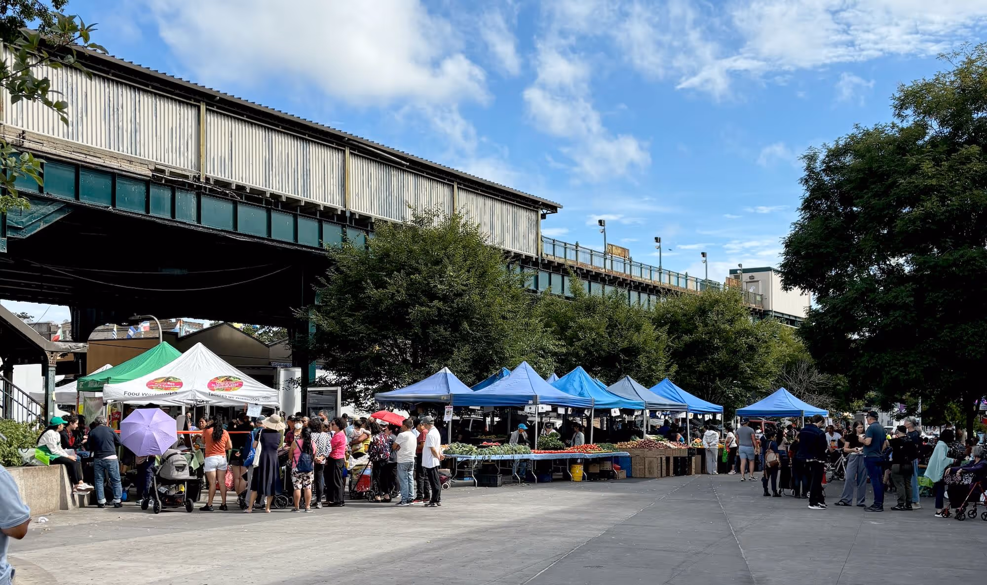 An outdoor farmers market is set up alongside an outdoor farmers market is set up with matching blue tents alongside an overground subway station