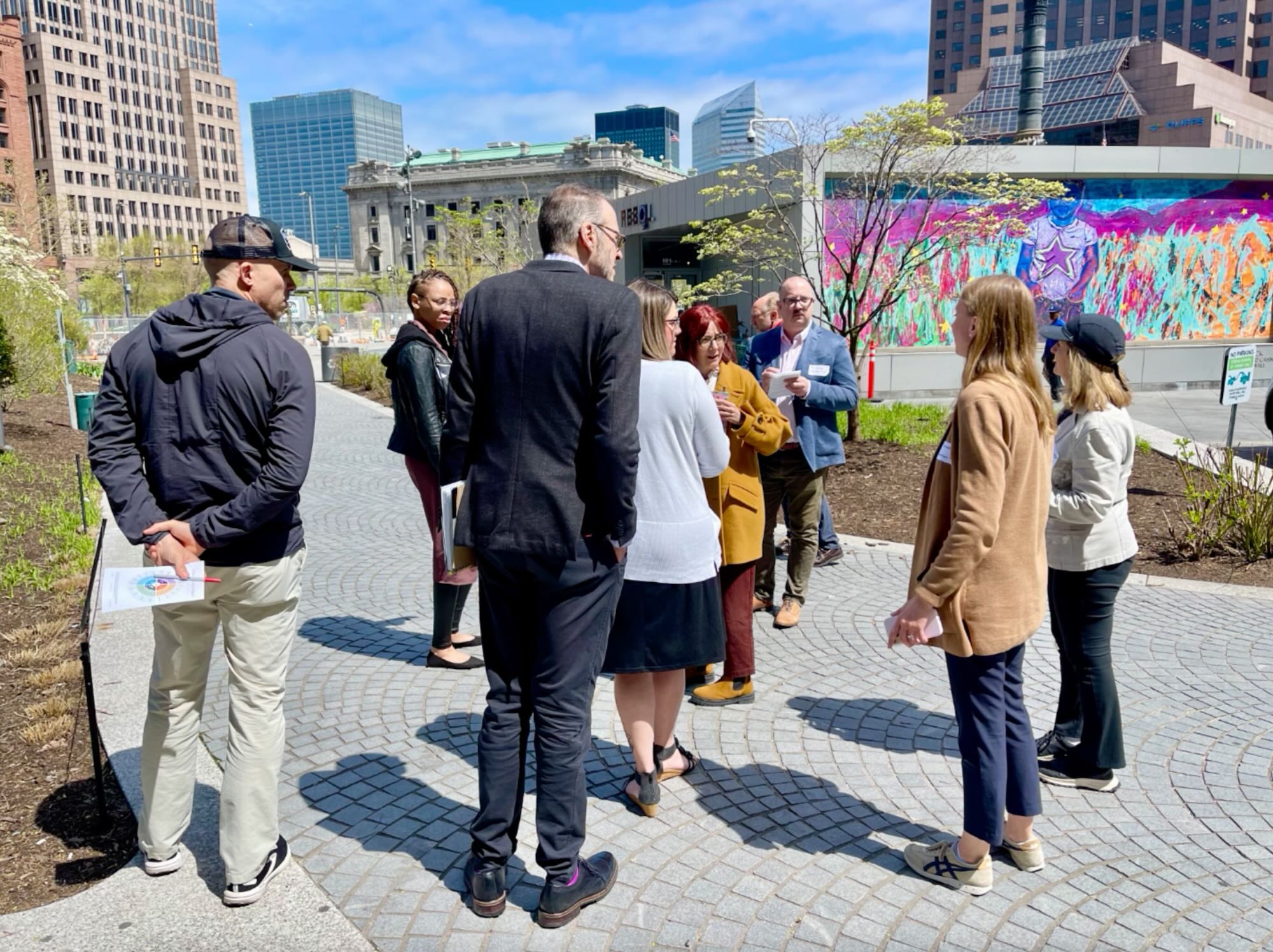 A group of adults are outdoors in a park setting with pens and papers in hand. 