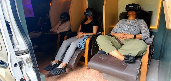 Three clients relaxing in massage chairs wearing Relax VR headsets inside the van