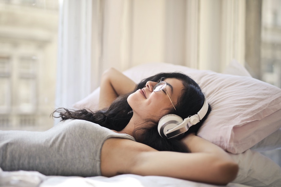 Woman listening to music with headphones while lying on bed