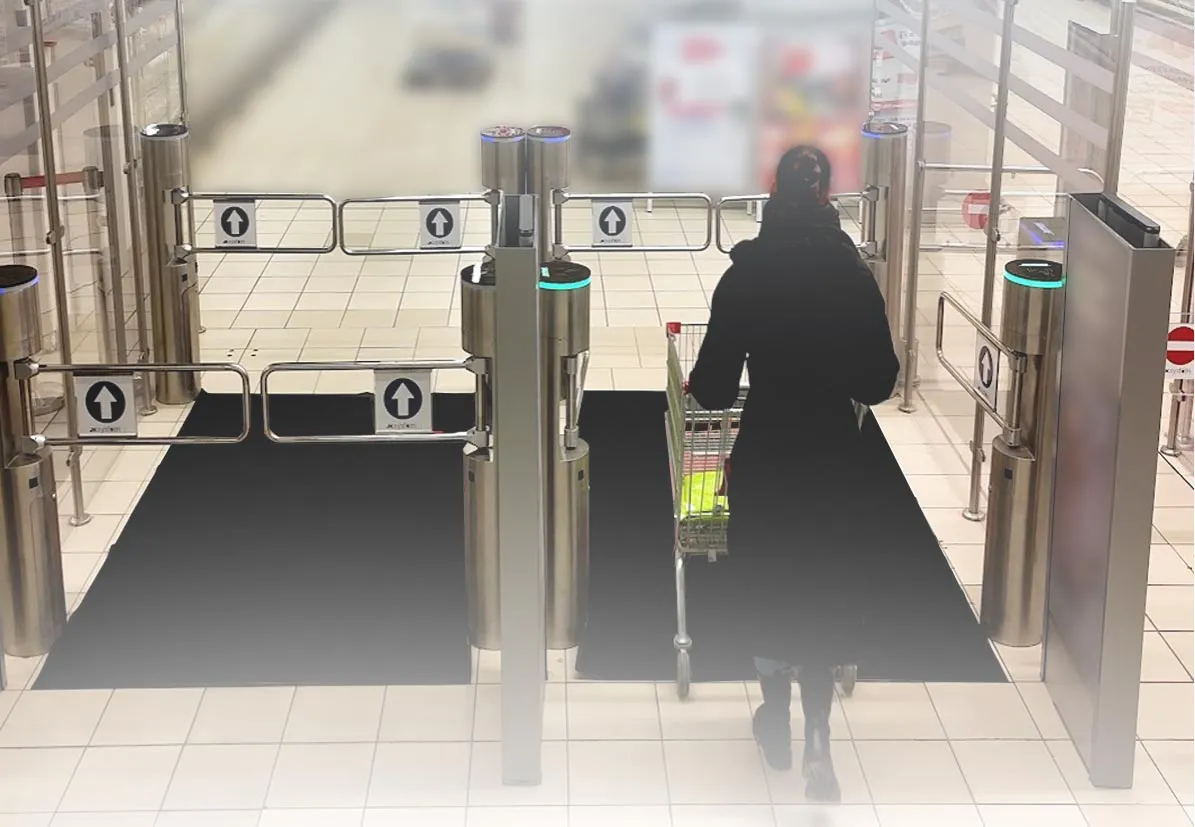 Person in a black coat pushing a shopping cart through retail entrance security gates.