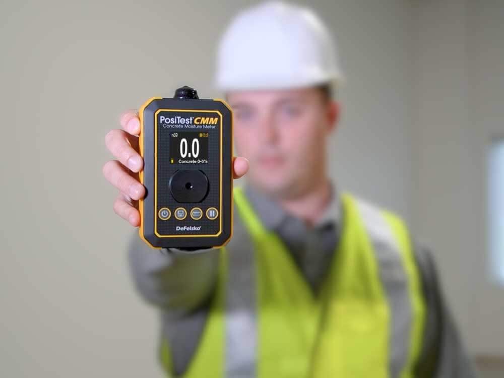 O PosiTest CMM Medidor de umidade do concreto sendo segurado por um homem com um colete de construção amarelo