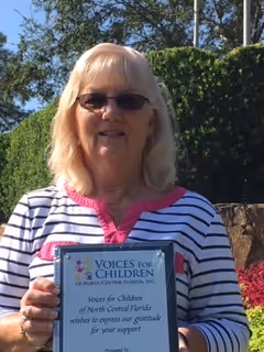 Photo of Paula Pombier holding a plaque from Voices for Chidlren