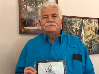 Wilbur Vanwyck holding up a plaque from Voices for Children of North Central Florida