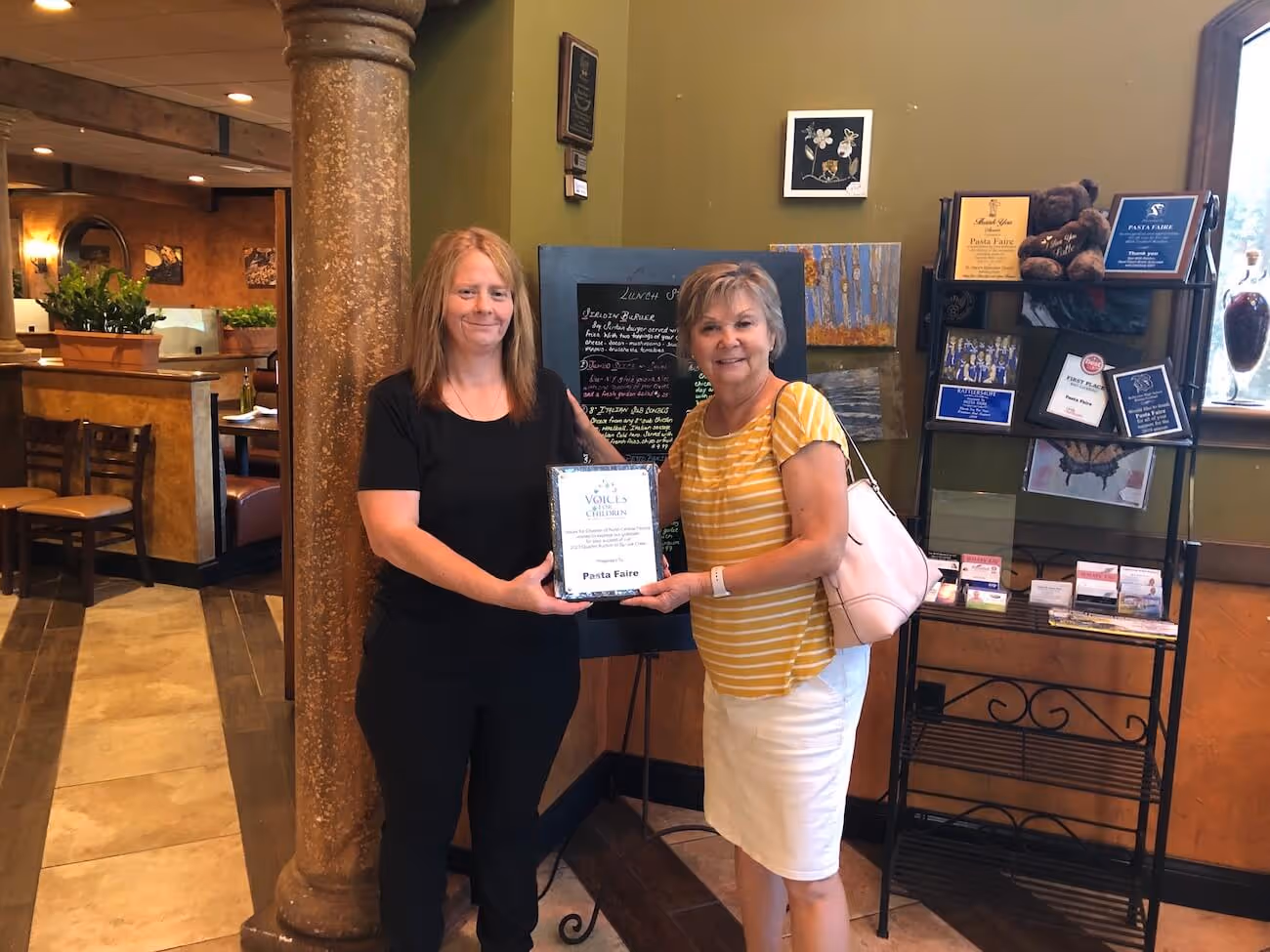Kathy Funk (r), General Manager of Pasta Faire in Belleview is presented a recognition plaque from Joan Knight of Voices for Children