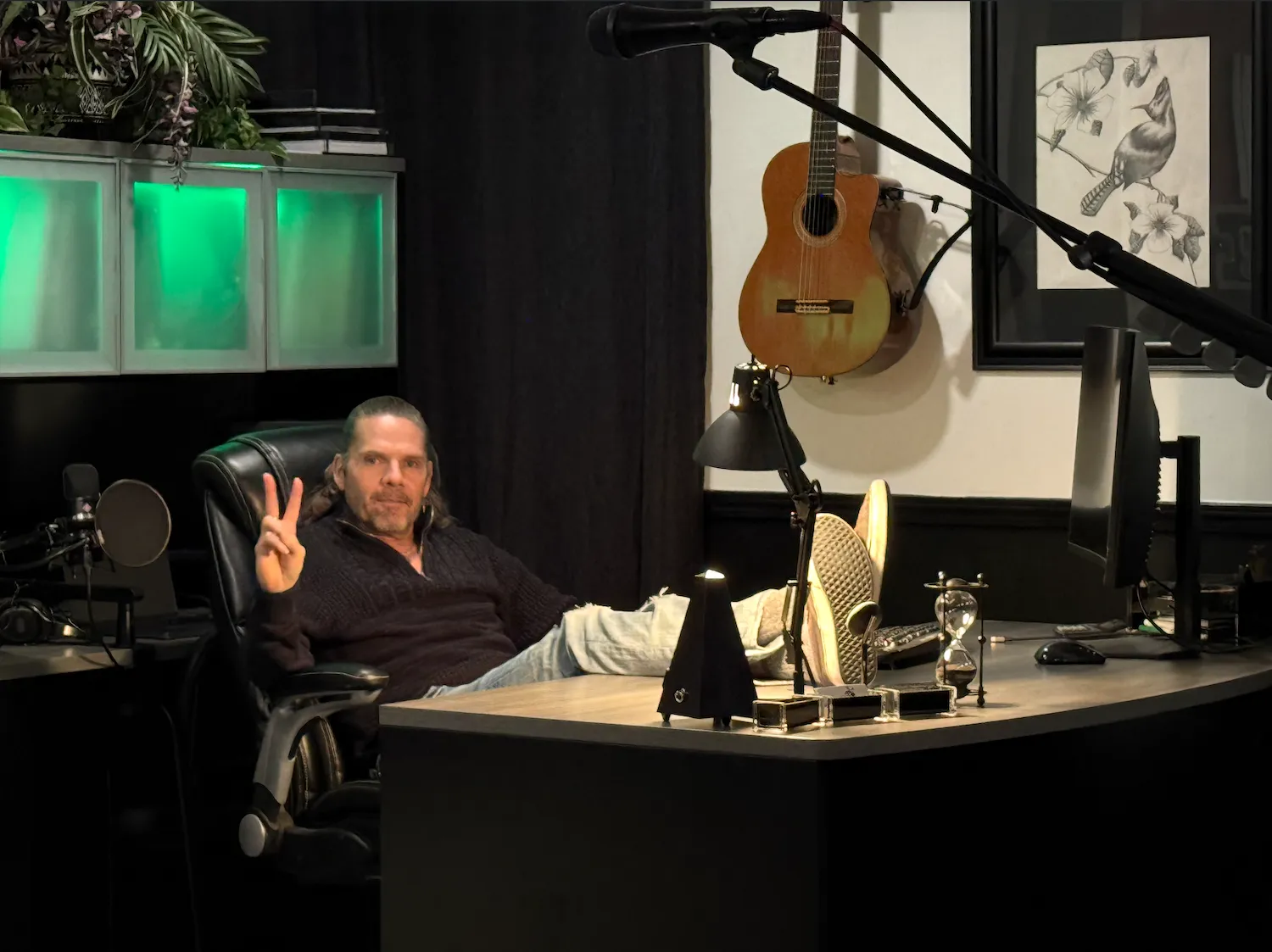 Man in a white shirt and blue jeans playing an electric guitar while leaning against a stone wall.