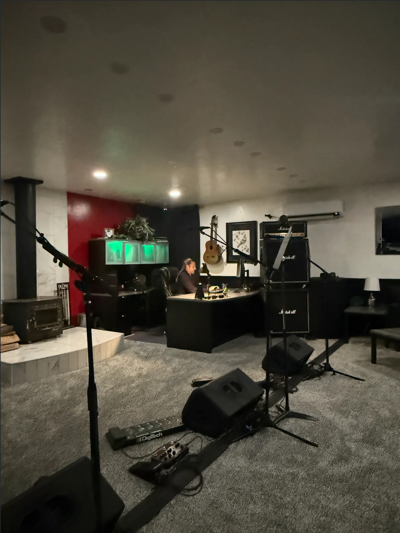 Man in a white shirt and blue jeans playing an electric guitar while leaning against a stone wall.