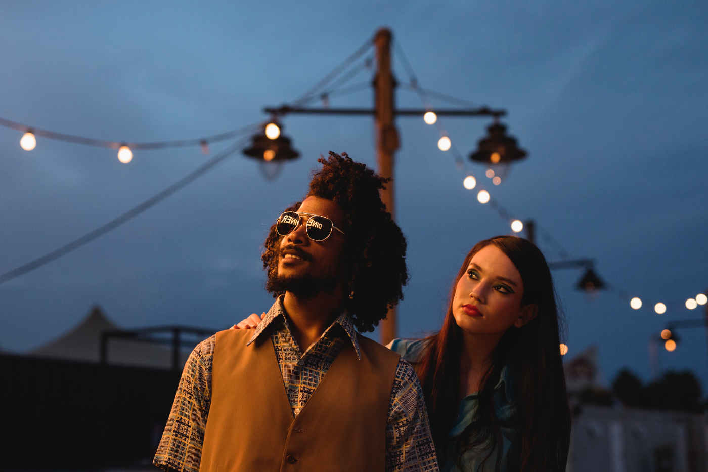 Man en vrouw poseren samen buiten in de avond met sfeerverlichting op de achtergrond