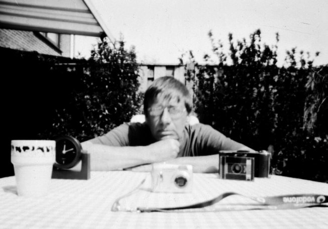 Foto van een zelfgebouwde pinhole-camera gemaakt van een theeblikje, met voorbeeldfoto en toelichting over belichting en werkwijze.