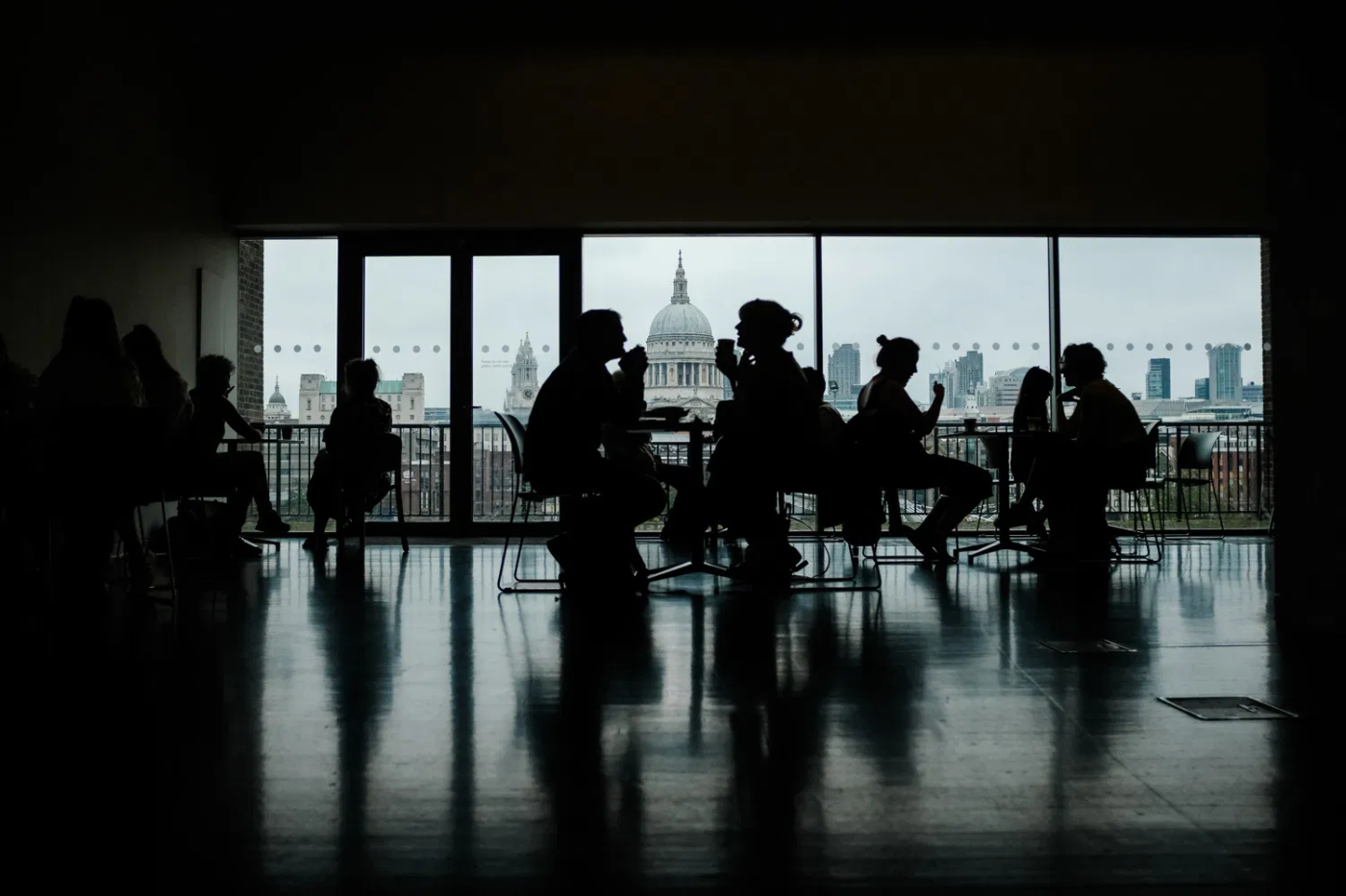 Silhouetten van mensen in een café, gefotografeerd bij weinig licht met uitzicht op de stad