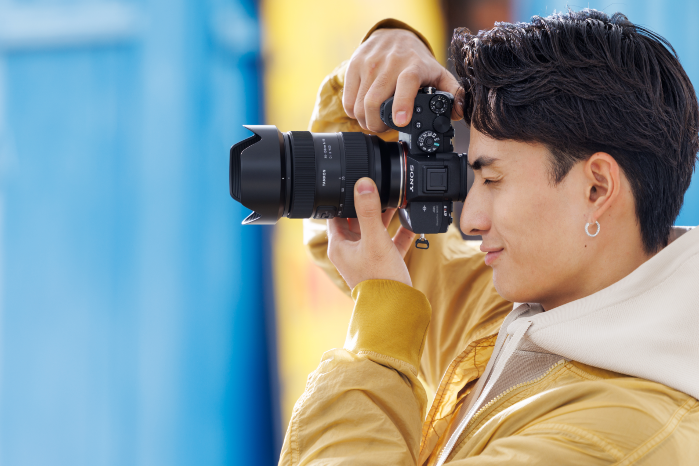 Fotograaf in profiel die een systeemcamera met Tamron zoomlens gebruikt, close-up van lens en houding