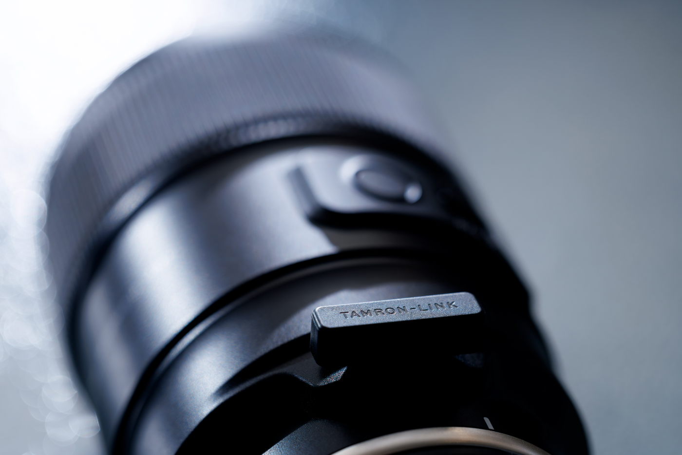 Close-up van de Tamron-LINK Bluetooth-adapter ingeplugd in de USB-C-poort van een Tamron-objectief.