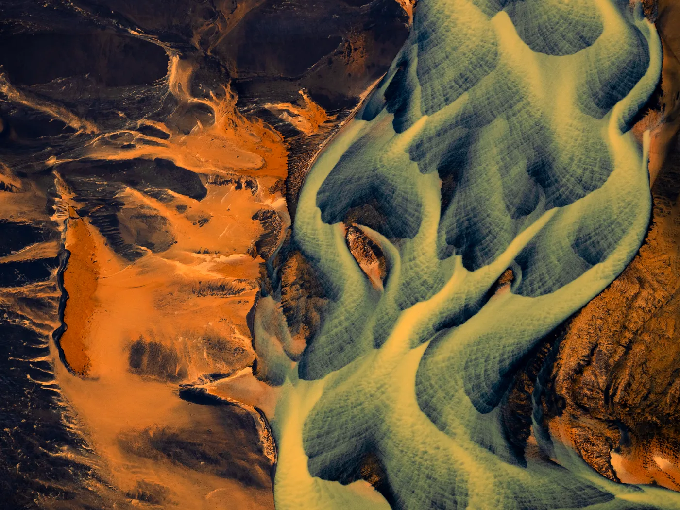 Luchtfoto van gevlochten gletsjerrivieren in zuidelijk IJsland, waar blauwgroene waterstromen zich tussen roestbruine en goudgele vulkanische sedimenten in abstracte patronen over het landschap verspreiden.