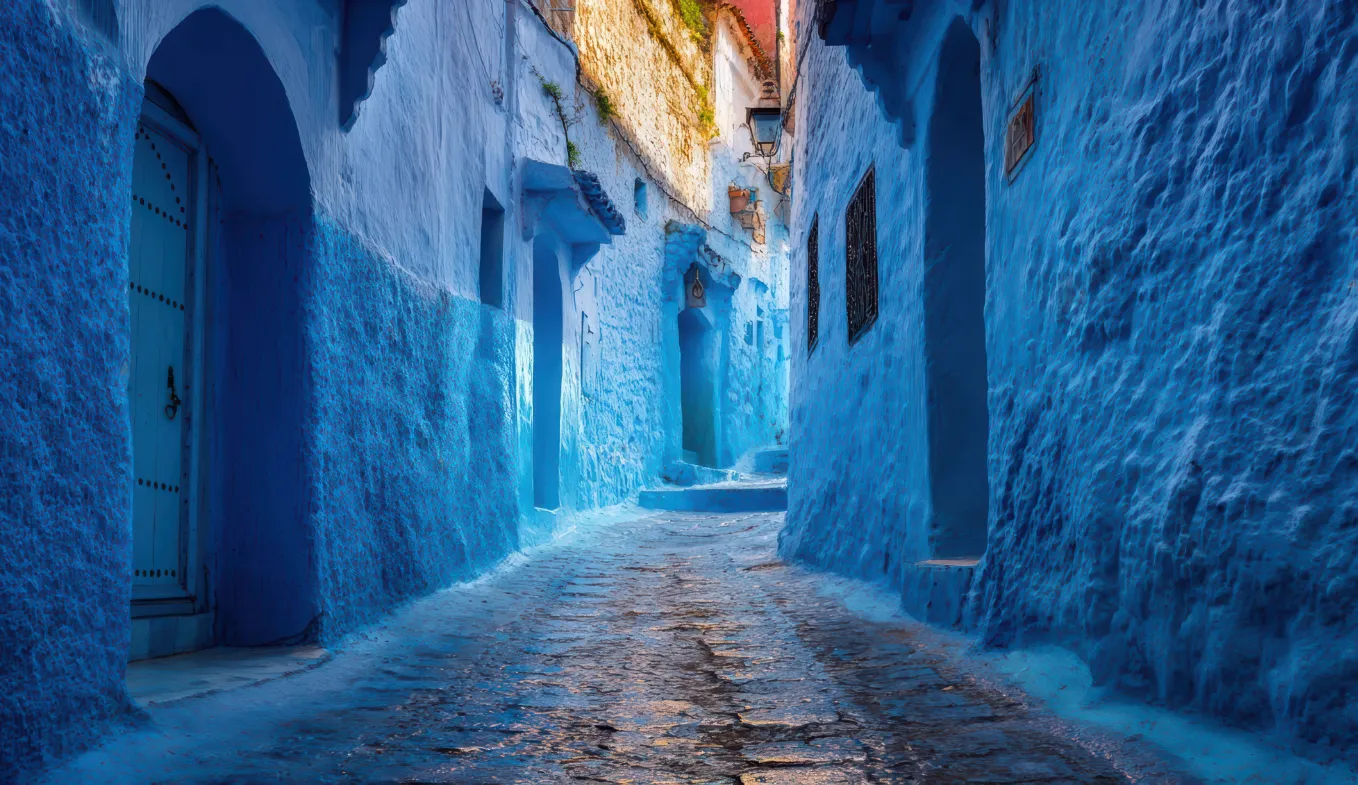 Smalle blauwe straat in het Marokkaanse Chefchaouen met felblauw geschilderde muren en karakteristieke bogen, populair bij reisfotografen.