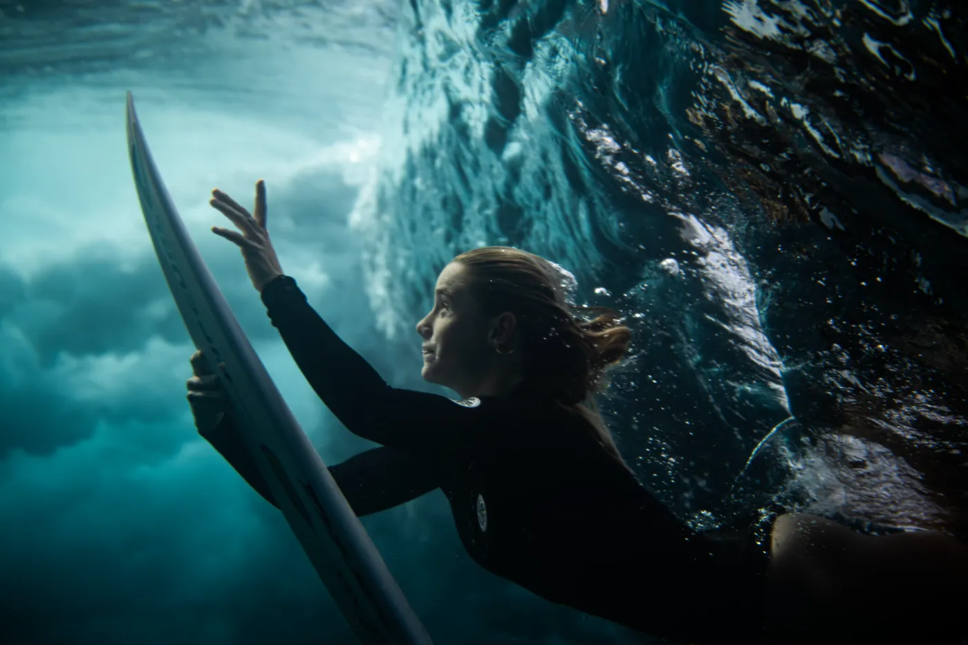 Surfer onder water naast haar surfboard, vlak onder een brekende golf in de bekroonde sportfoto The Underworld van Beatriz Ryder Da Costa.