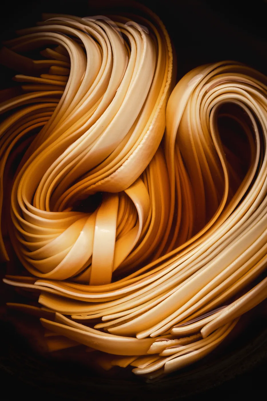 Close-up van sierlijk gevouwen noodles in warm licht tegen een donkere achtergrond.