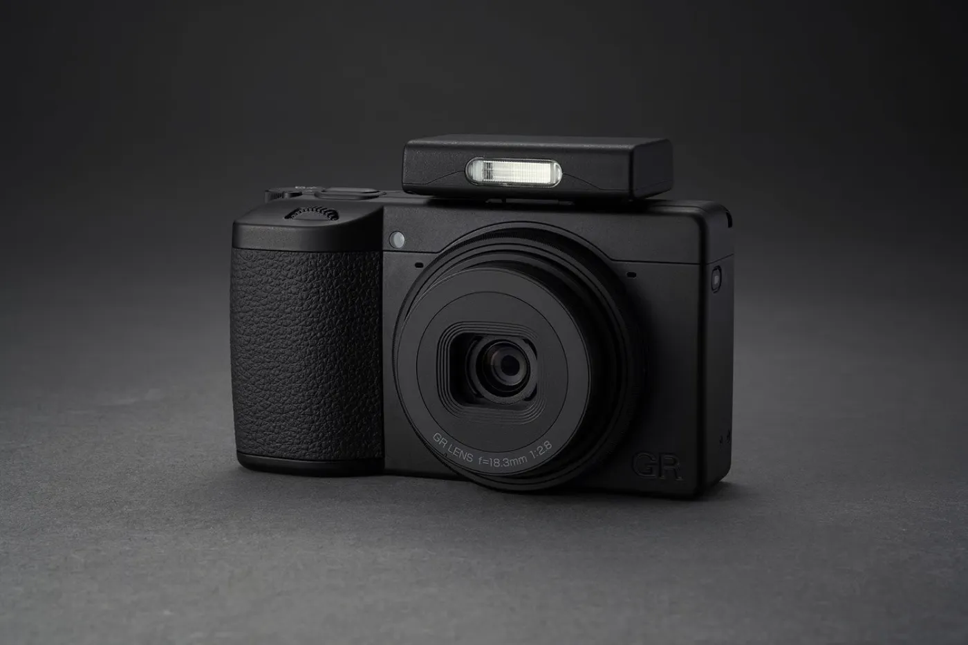 Ricoh GR IV Monochrome van voren gezien met externe flitser op een donkere ondergrond