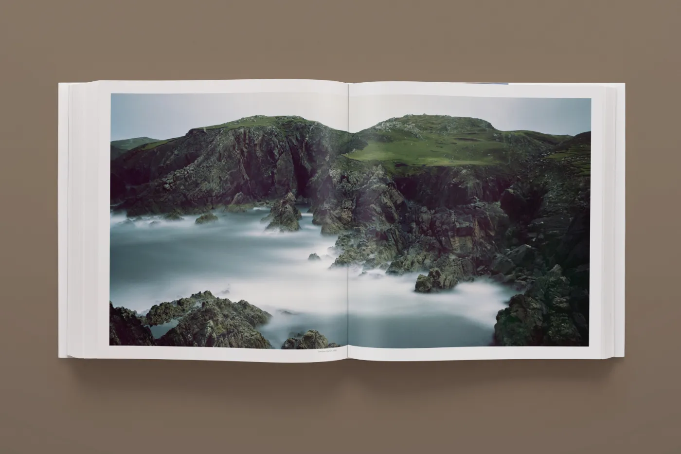 Open boek met een foto van een rotskust en gladgetrokken water uit Darren Almonds Fullmoon-serie