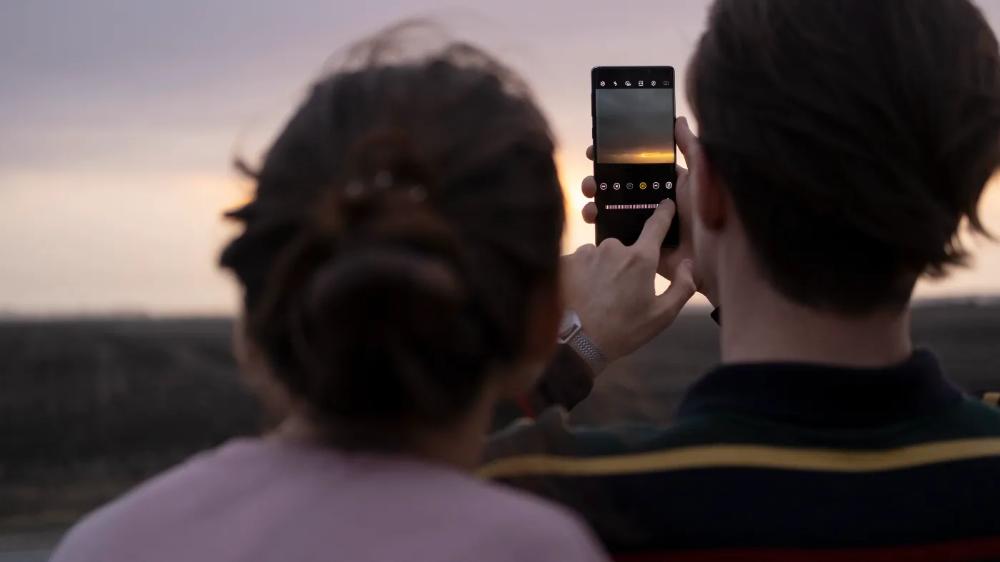 Twee mensen fotograferen een zonsondergang met een smartphone.