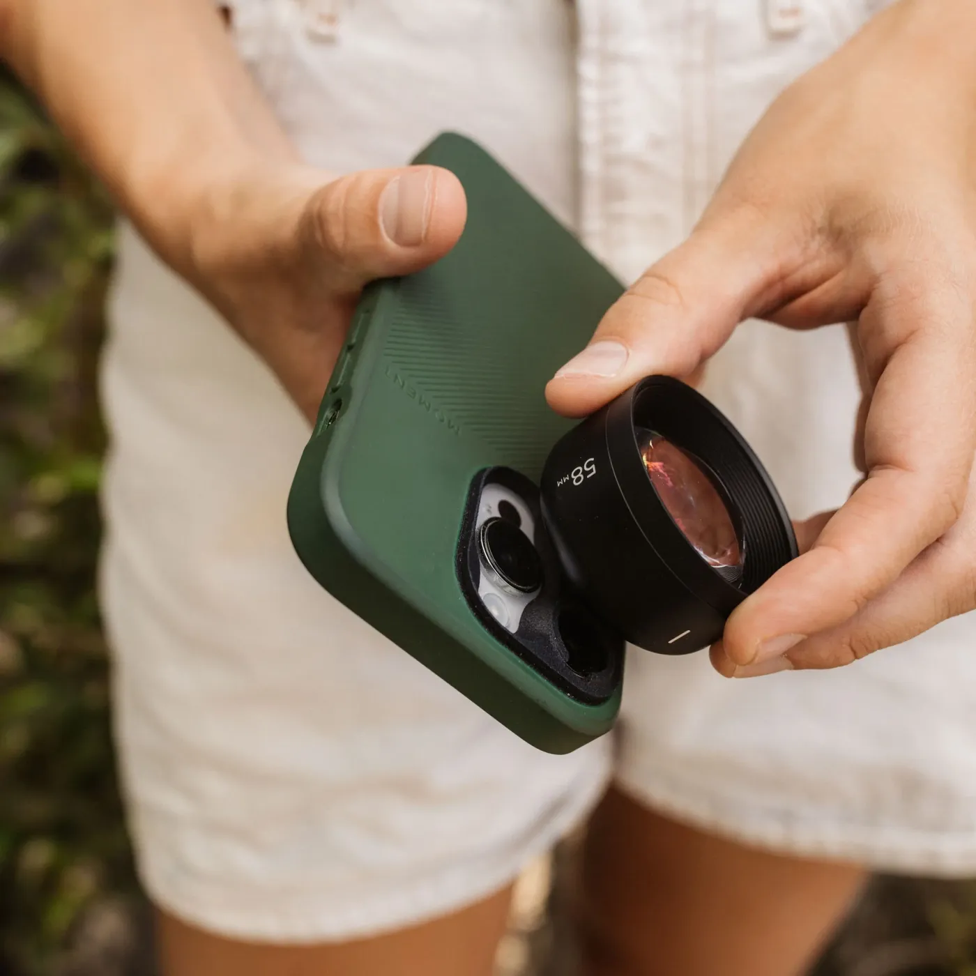 Hand bevestigt een zwarte 58mm-telelens op een groene smartphone