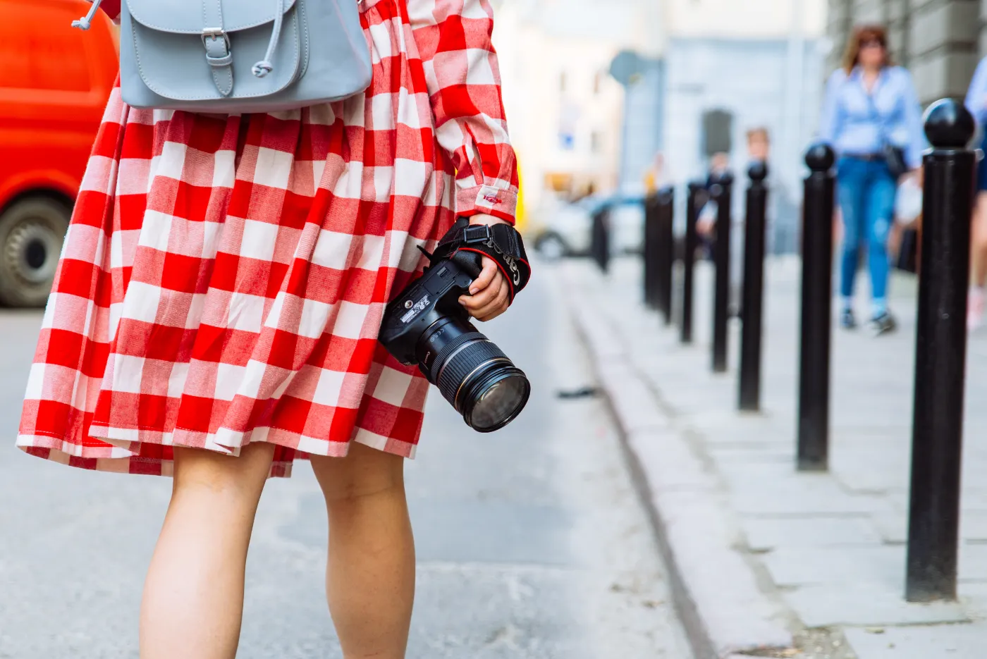 Vrouw in geruite jurk loopt door de stad met een camera in haar hand