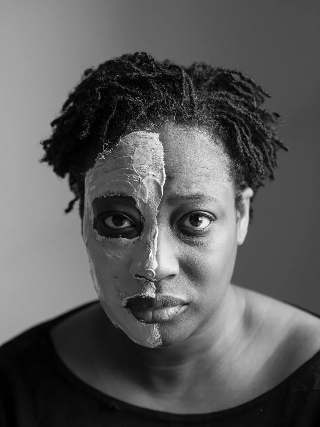 Zwart-witportret van een vrouw met één helft van haar gezicht met een beauty kleimasker
