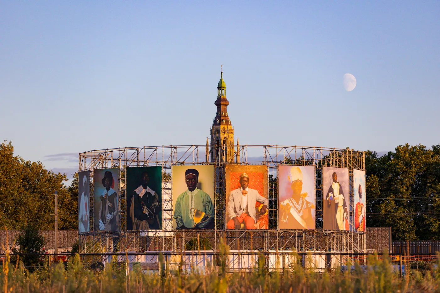 BredaPhoto-installatie met grote portretten op een stellage voor een kerktoren in avondlicht