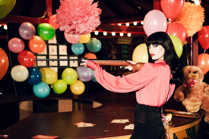 Model in roze blouse in een kleurrijke circusachtige setting met ballonnen.