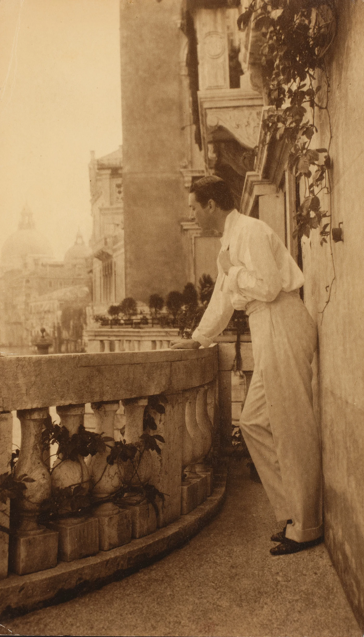 Sepiakleurig portret van Adolphe de Meyer, staand op een balkon van Palazzo Balbi-Valier in Venetië.