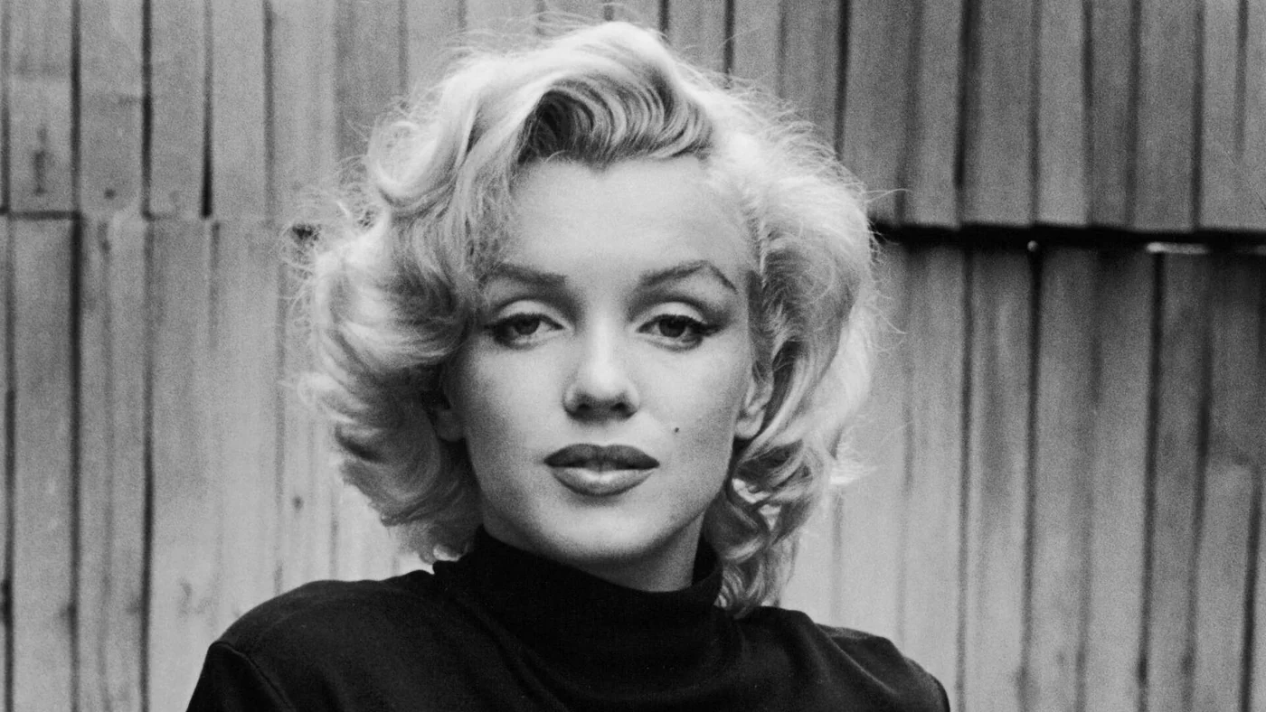 Zwart-witportret van Marilyn Monroe met blond haar voor een houten achtergrond.