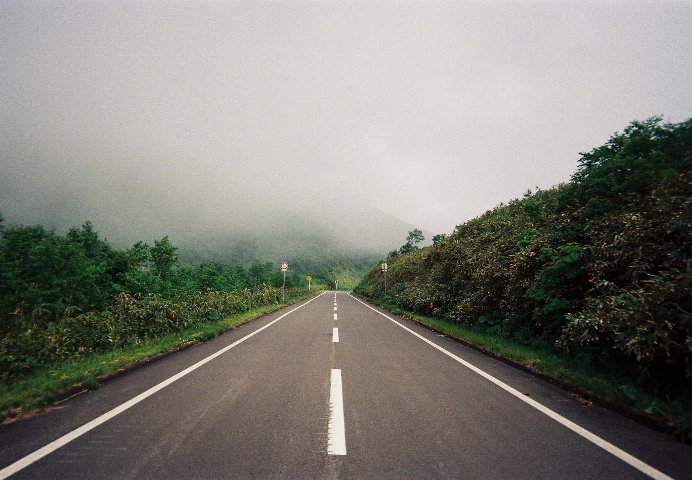 Analoge voorbeeldfoto van een lege weg tussen groen en mistige heuvels.