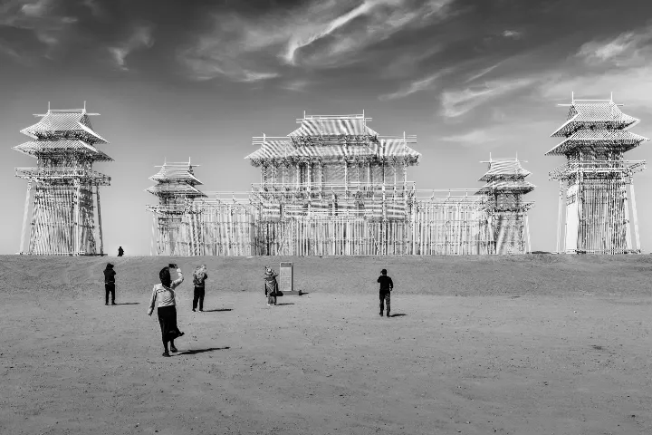 Zwart-witfoto van een monumentale, op Chinese paleisarchitectuur geïnspireerde constructie in een open landschap, met enkele bezoekers op de voorgrond.