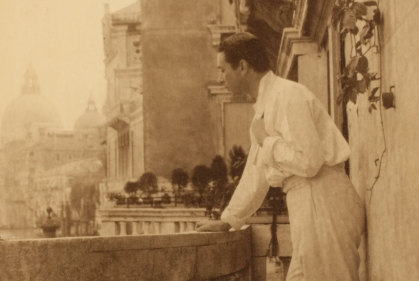 Sepiakleurig portret van Adolphe de Meyer, staand op een balkon van Palazzo Balbi-Valier in Venetië.