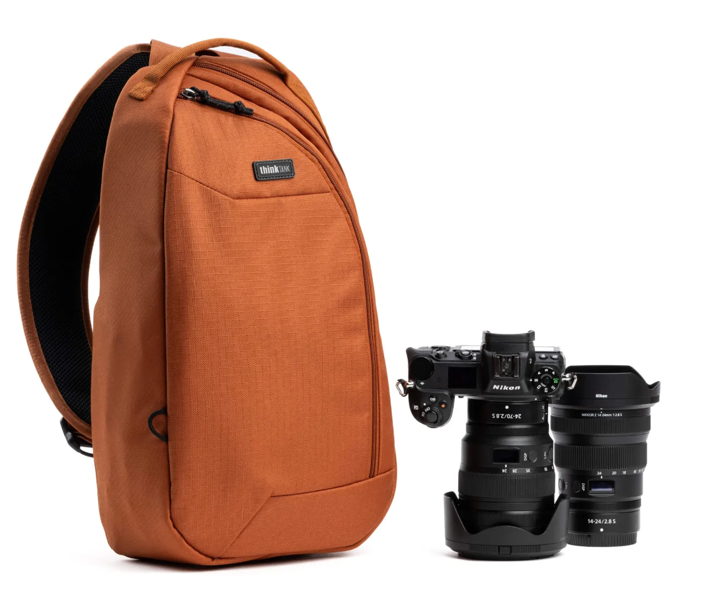 Roestbruine Think Tank TurnStyle-slingtas naast een Nikon-camera en twee objectieven.