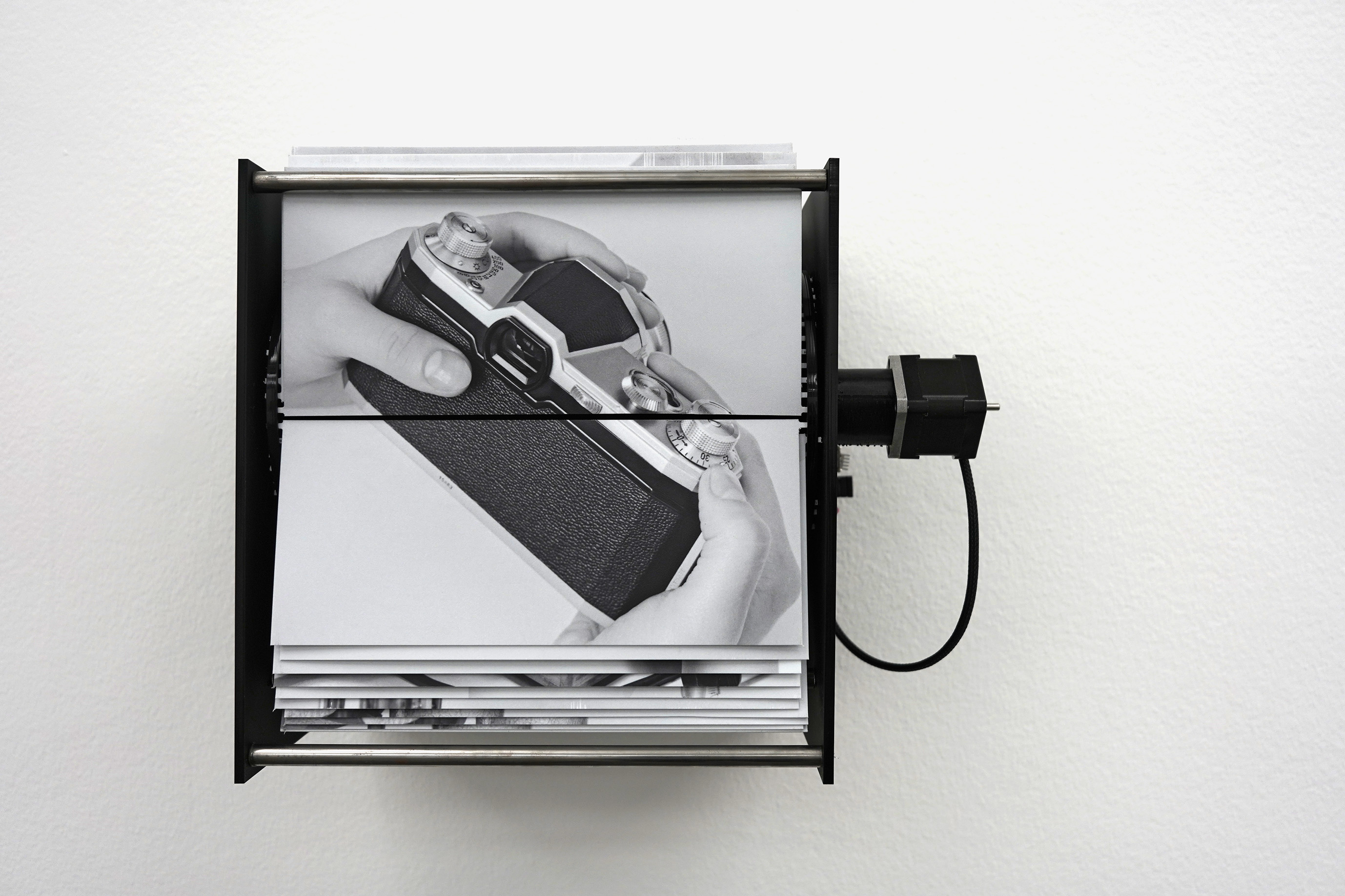 Installatiebeeld van Isabelle Le Minhs Raw Loop met een zwart-witfoto van handen met een camera op een ronddraaiende display.