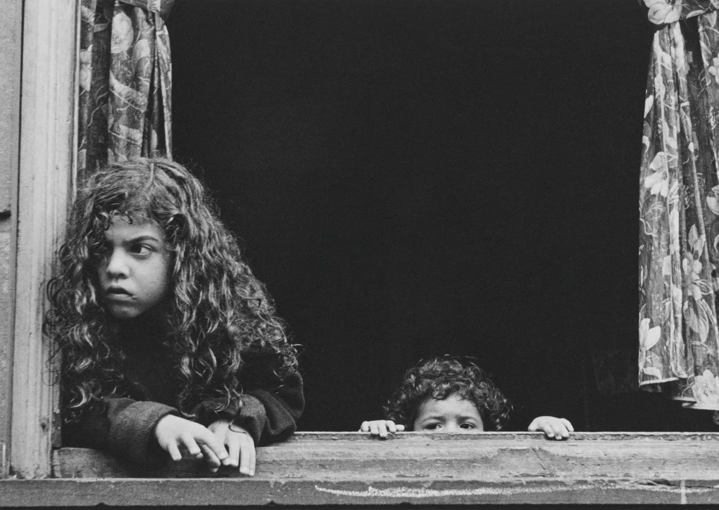 uit de tentoonstelling Helen Levitt: City at Play in Kunsthal Rotterdam.: zwart-witfoto van twee kinderen die vanuit een donker raam naar buiten kijken
