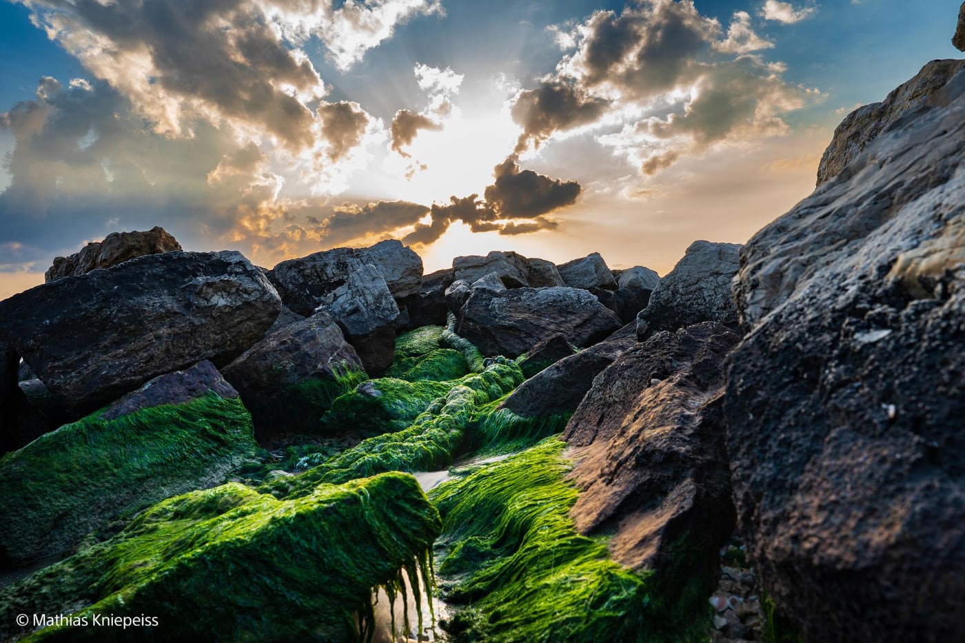 Rotsachtige kust met groene algen en zonlicht achter wolken