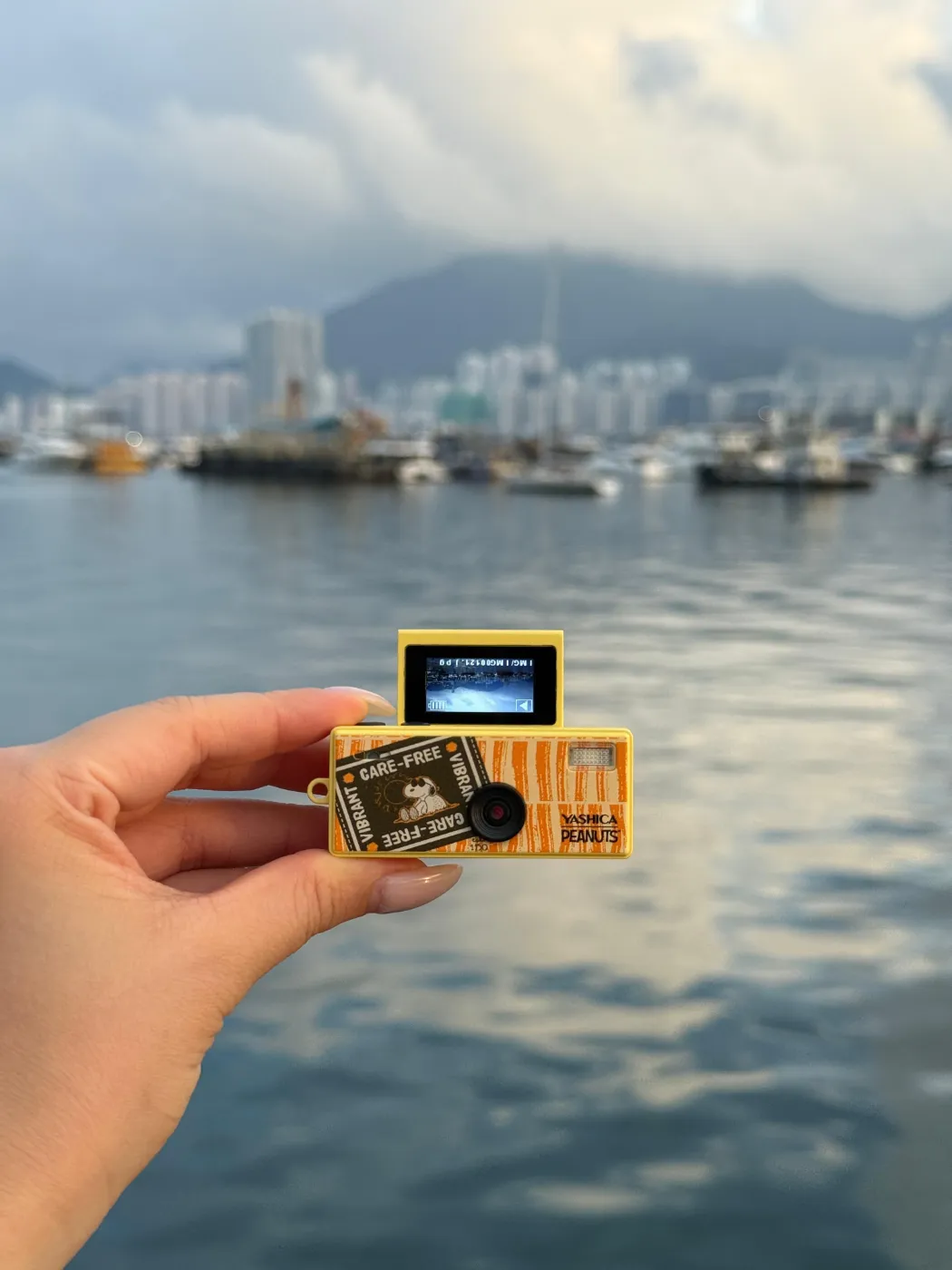 Yashica x Peanuts Funtastic Keychain Camera in de hand met haven op de achtergrond