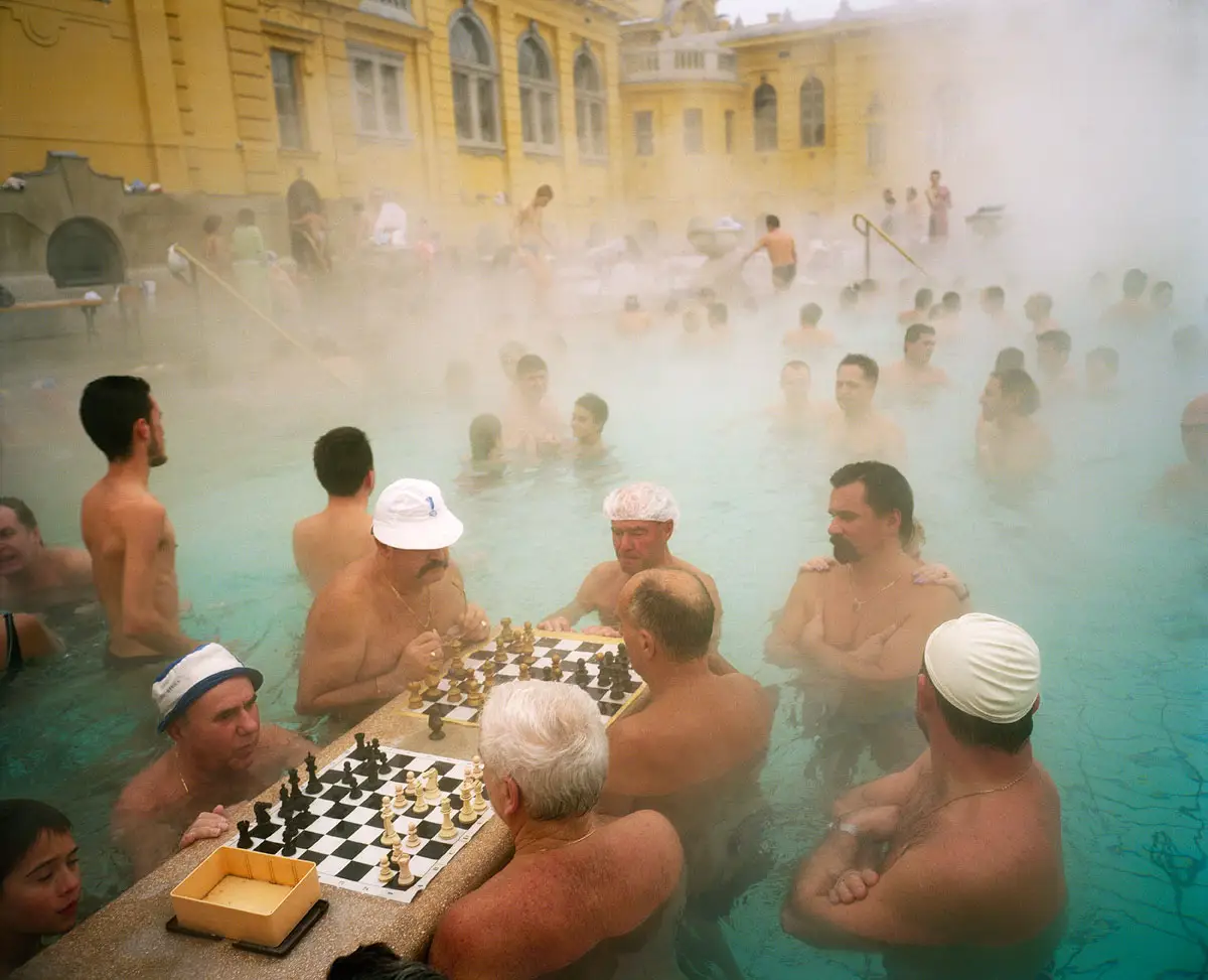 Mensen zitten in een stomend buitenbad en spelen schaak aan de rand van het water