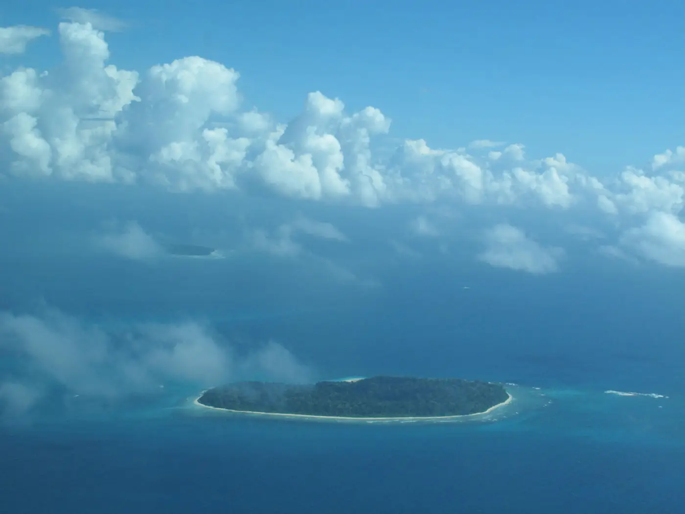 Luchtfoto van een klein groen eiland in blauwe zee onder hoge wolken