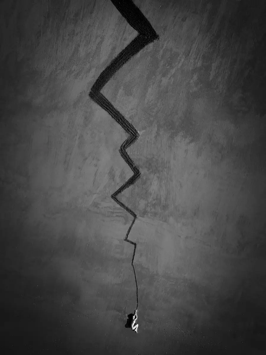 Zwart-wit luchtfoto uit Aerial Bodies van Ruben Bellanger, met een kleine naakte figuur onderaan een uitgestrekt landschap en een lange zigzaglijn door het beeld.