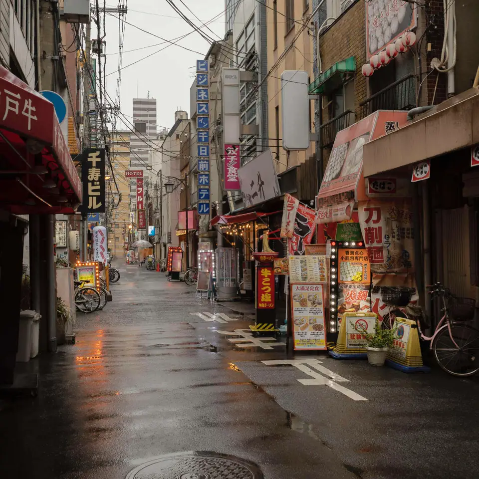 Natte straat in Japan met verlichte gevels en reflecties na een regenbui.