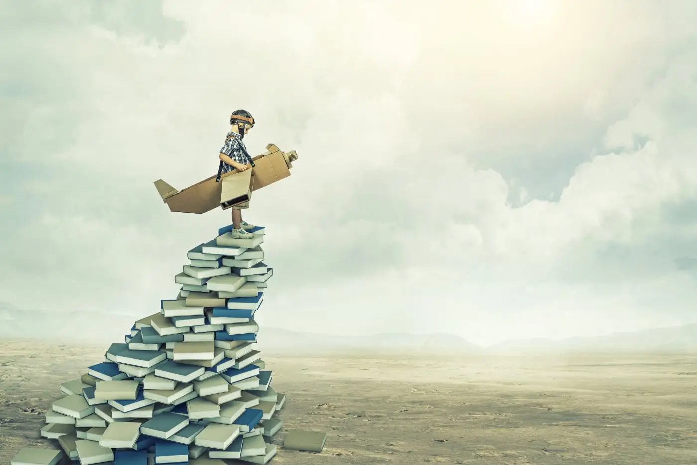 Jongen met kartonnen vliegtuig staat boven op een hoge stapel boeken