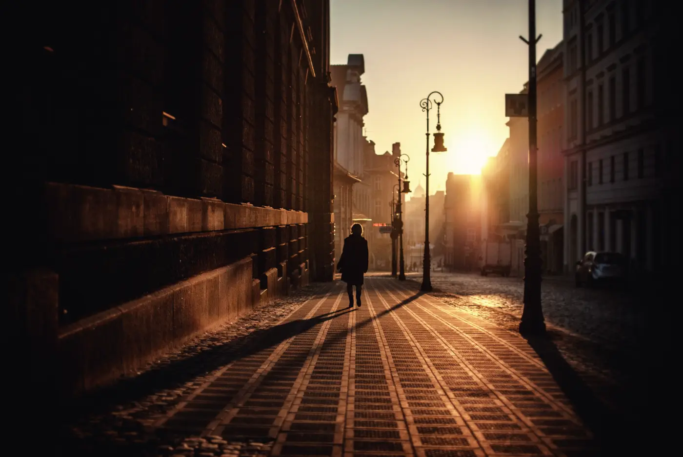Vrouw loopt over straat in warm avondlicht, gefotografeerd bij weinig licht