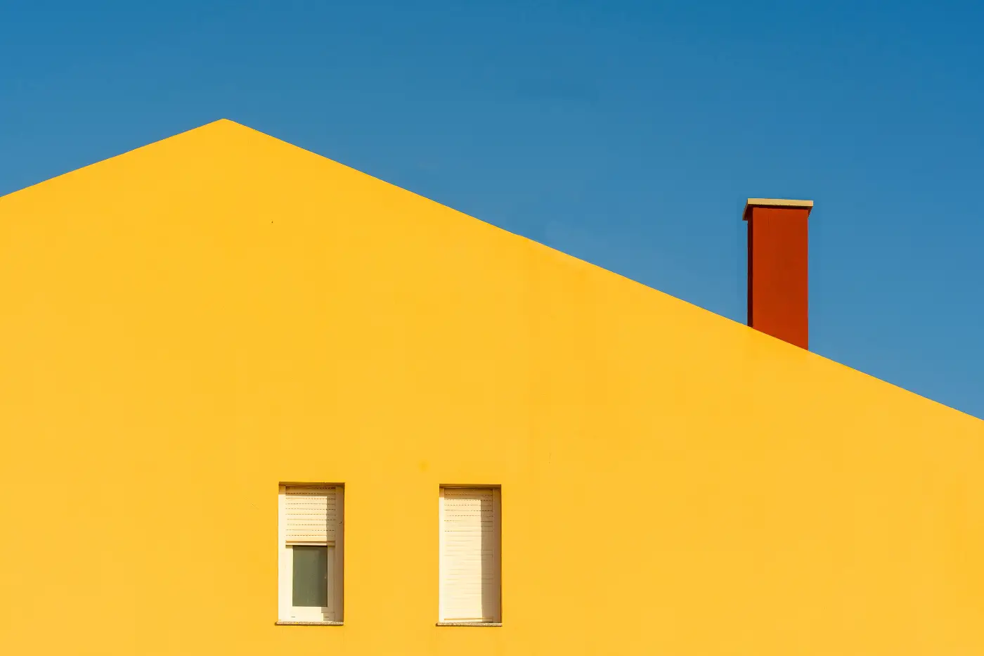 Minimalistische foto van gele gevel tegen blauwe lucht met rood kleuraccent