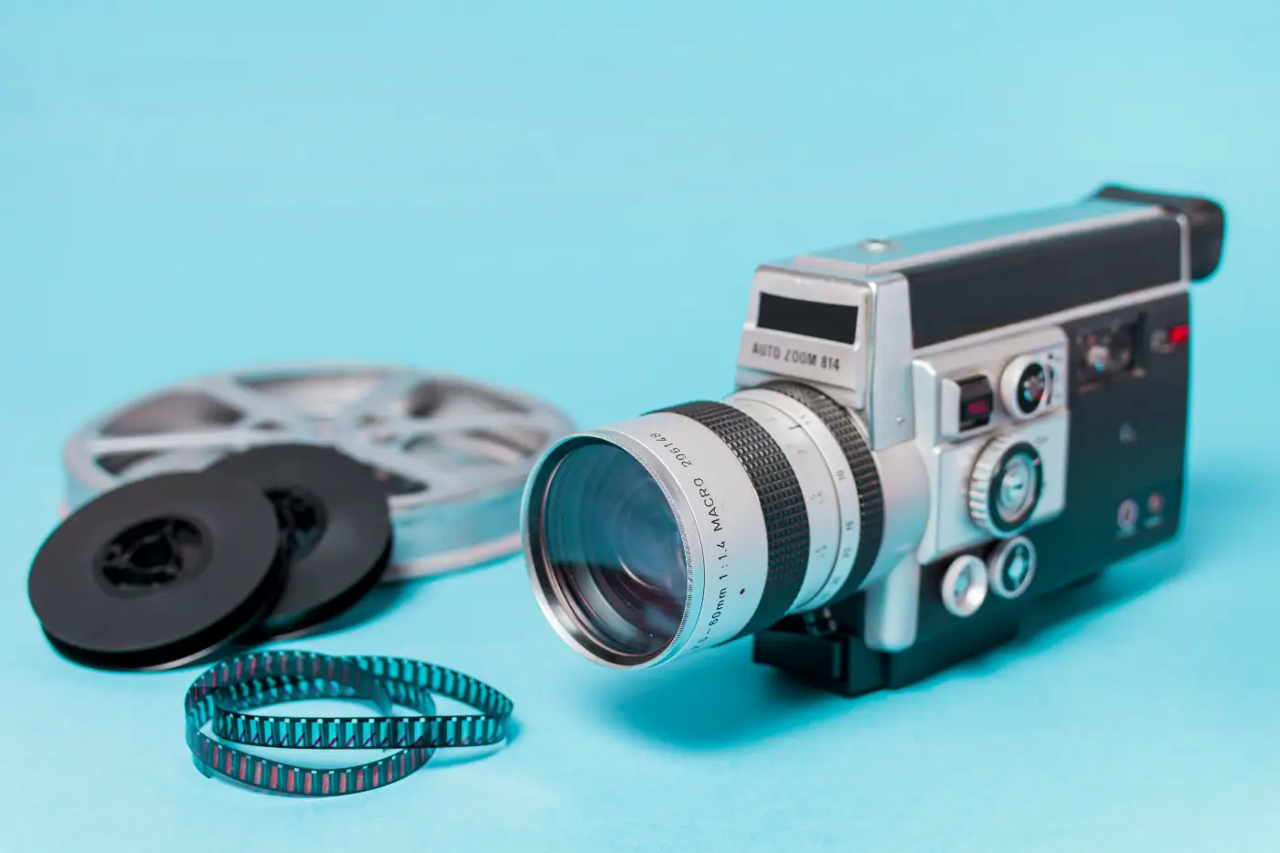 Vintage 8mm-filmcamera met filmspoelen en een losse filmstrook op een blauwe achtergrond.