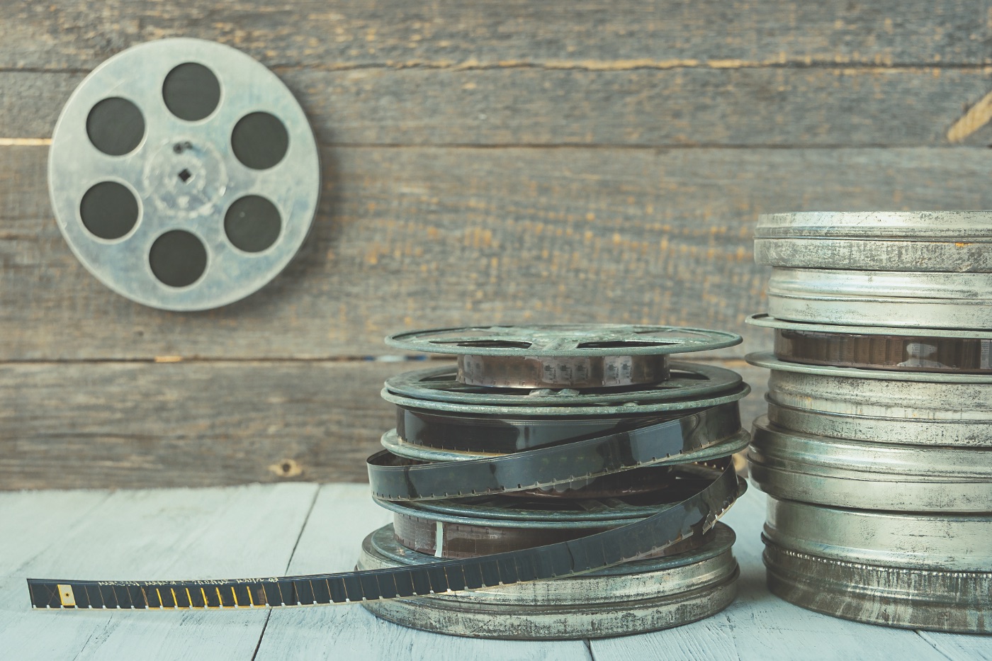 Oude filmspoelen en metalen filmblikken met een uitgerolde filmstrook op een houten tafel.